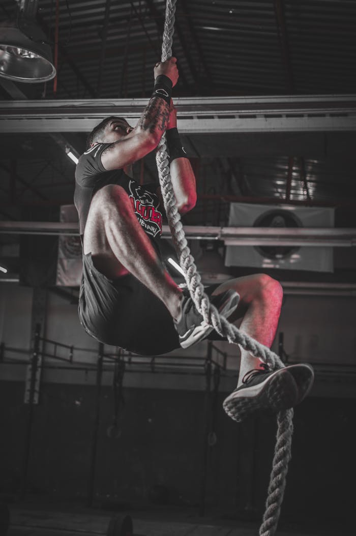Homme grimpant à la corde dans un hangar de crossfit faiblement éclairé